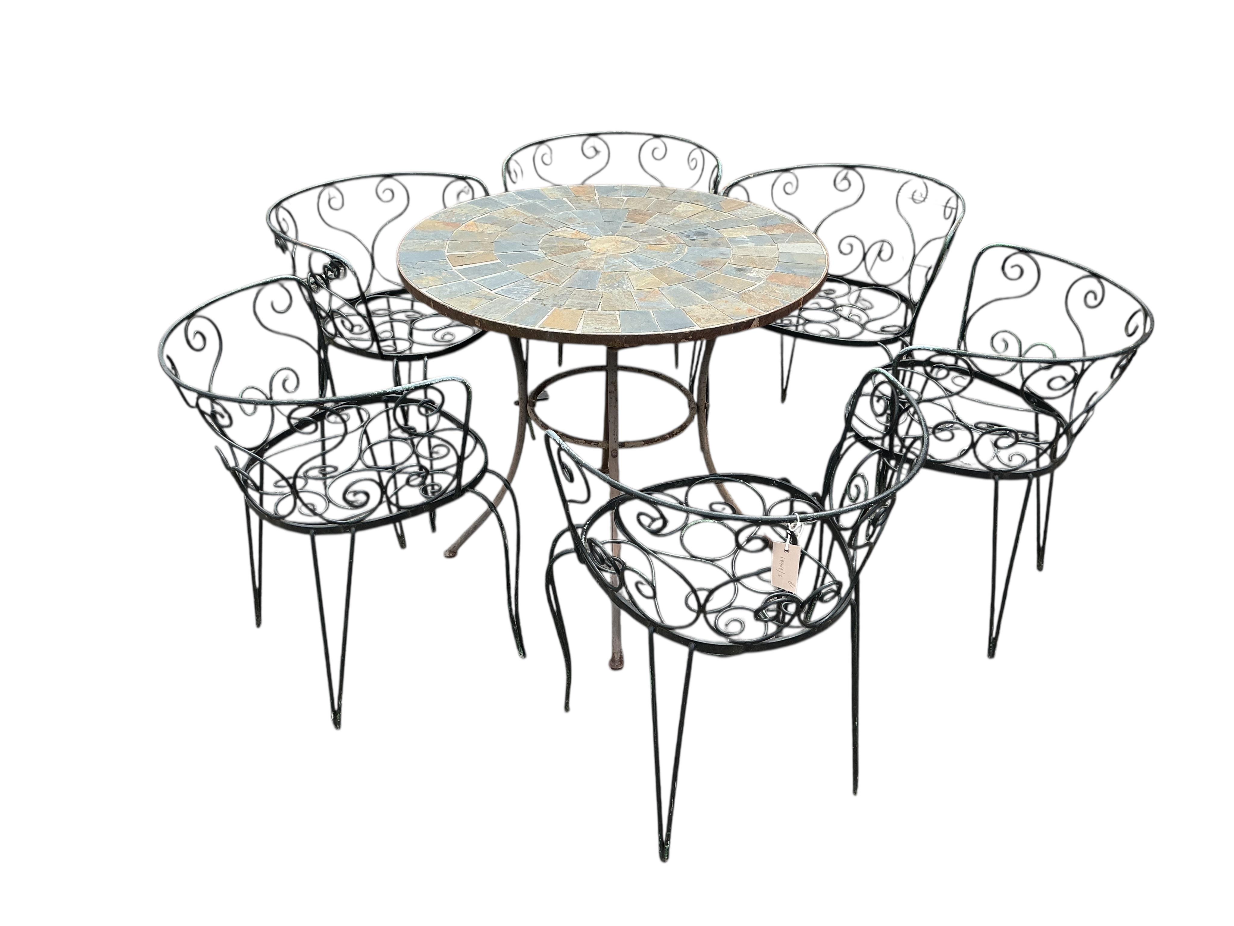 A circular stone mosaic topped garden table, diameter 80cm, height 72cm and six wrought iron garden chairs